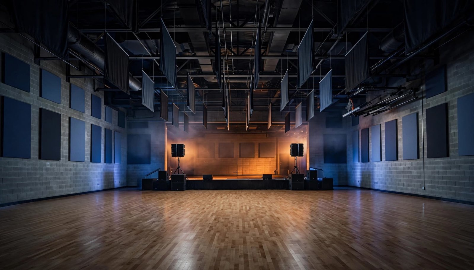 Empty school gym with speakers, acoustic panels, and blue and amber lighting.
