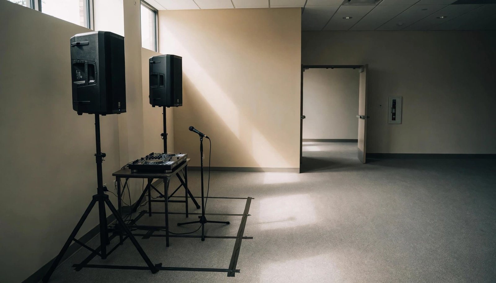 Two speakers, a DJ controller, and a microphone are arranged in an empty conference room.