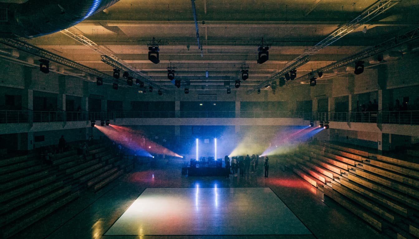 A DJ booth lights up a school gym dance floor with colorful beams.